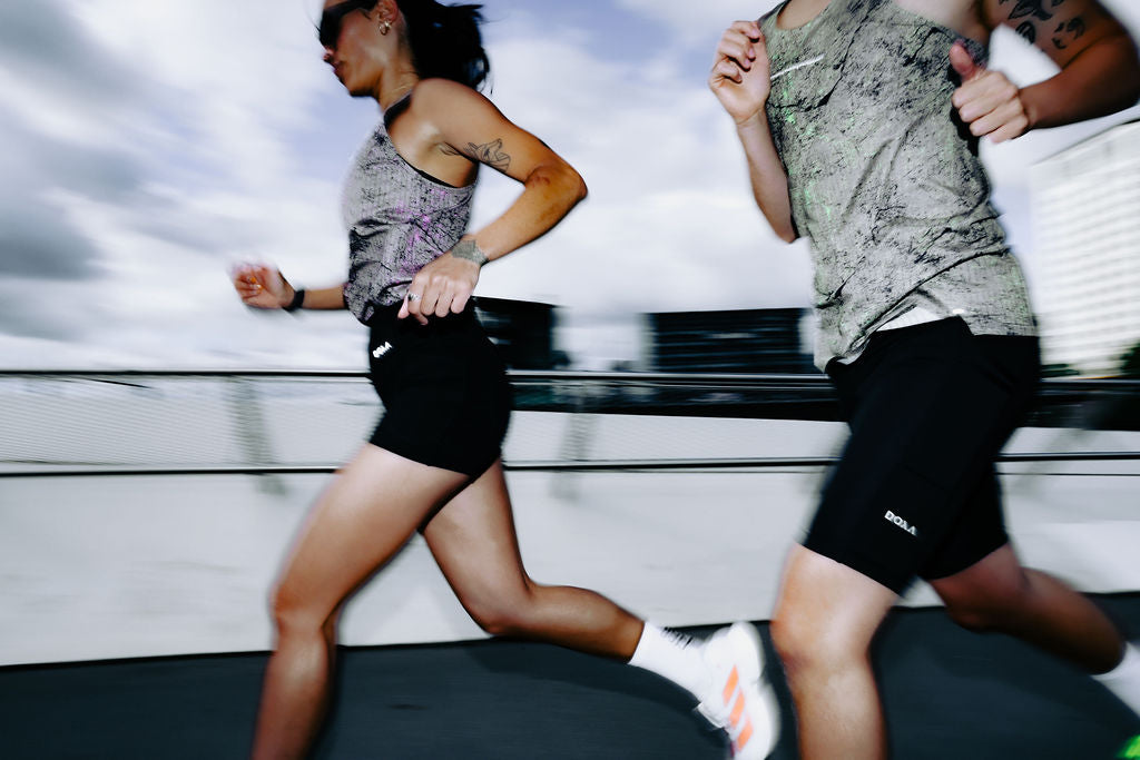 Two runners mid-stride wearing DOXA RErun mist-print singlet and tee with black running shorts - performance running apparel from Copenhagen