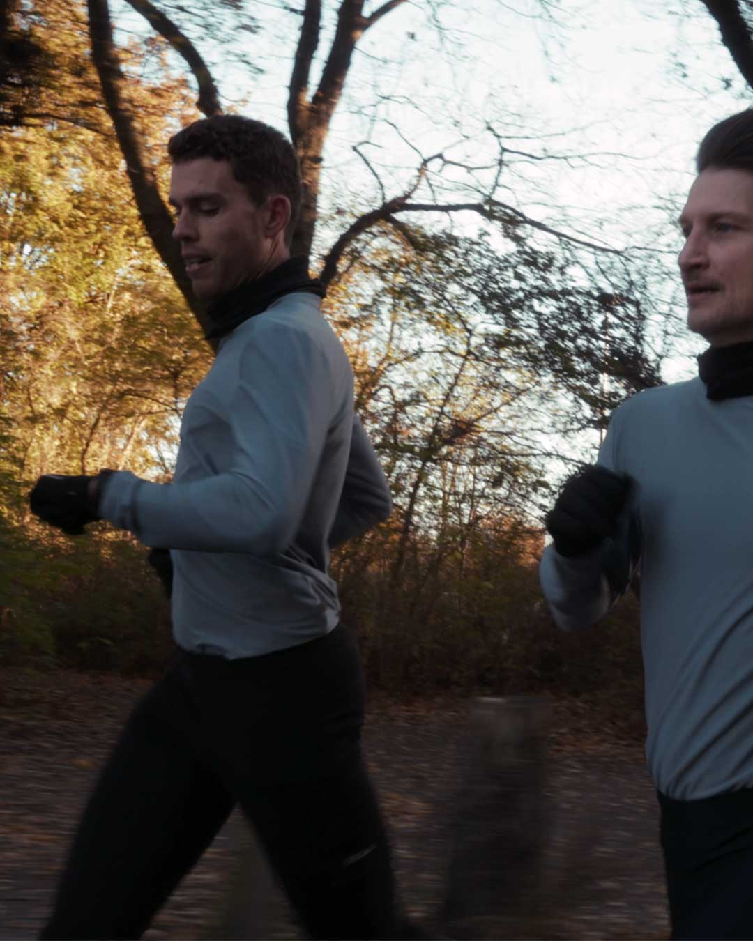 Two men running outdoors in a forested area during autumn wearing running apparel from DOXA RUN.